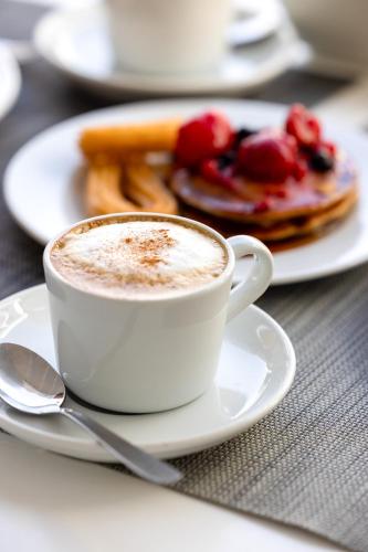 a cup of coffee sitting on a plate with pancakes at Corralejo Surfing Colors Hotel&Apartments in Corralejo