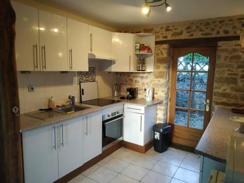 une cuisine avec des armoires blanches, un évier et une fenêtre dans l'établissement Petite maison à la campagne, à La Selle-Craonnaise