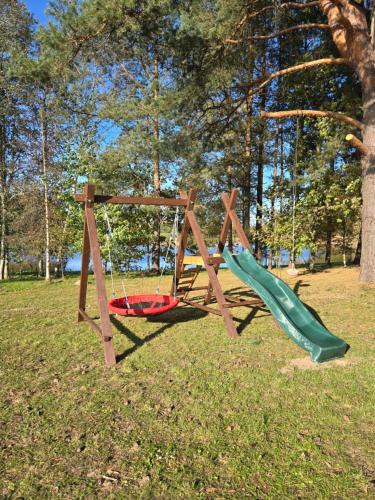 a swing set in a park with a green slide at Līdumnieki in Vērgale