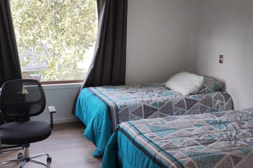 Un dormitorio con dos camas y una silla y una ventana. en Hermosa casa en parcela, en Puerto Varas