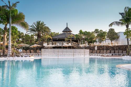 a pool at a resort with palm trees and umbrellas at Labranda Alyssa Suite Hotel in Playa Blanca