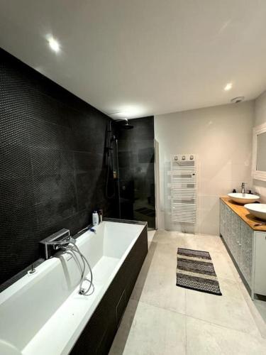 La salle de bains est pourvue d'une baignoire blanche et d'un mur noir. dans l'établissement Villa familiale avec piscine chauffée, à Périgny