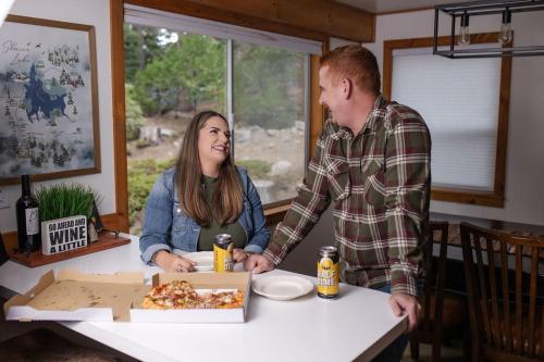 a man and a woman standing at a table with a box of pizza at Buckeye Bear's Den-ac-walking Distance To Town in Shaver Lake