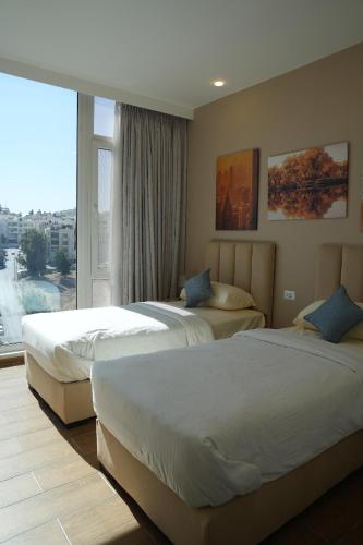 two beds in a hotel room with a large window at Janty Apartments in Amman