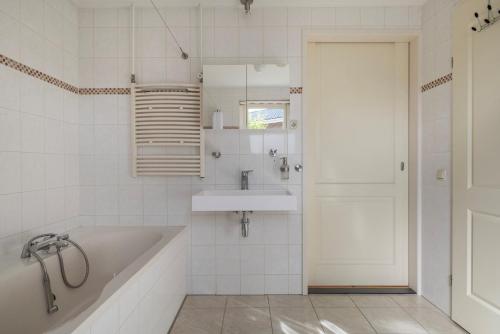 a white bathroom with a tub and a sink at Komfortables Ferienhaus mit Garten, Weitblick und Whirlpool in Tzummarum