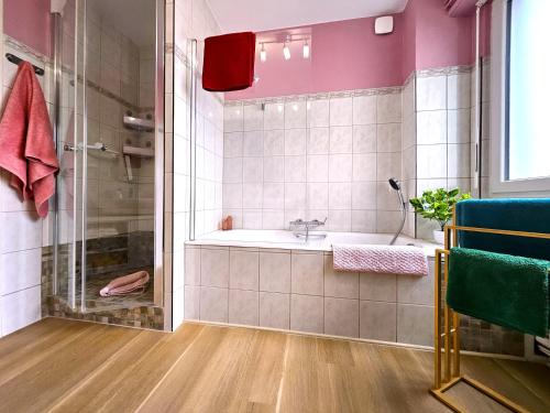 La salle de bains est pourvue d'une baignoire et d'une douche aux murs roses. dans l'établissement Charmant T4- Centre Ville- Parking Privé, à Colmar