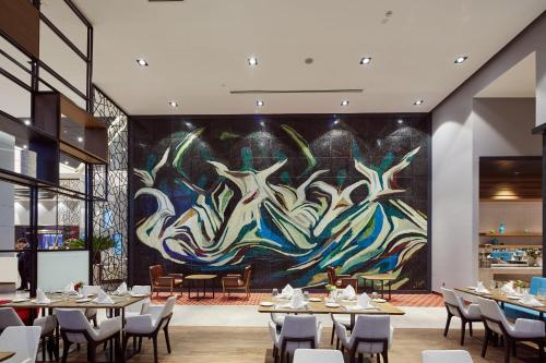 a restaurant with tables and a large painting on the wall at Novotel Konya in Konya