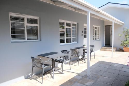 a patio with tables and chairs on a white house at High Hedges Guest Suites Constantia in Cape Town