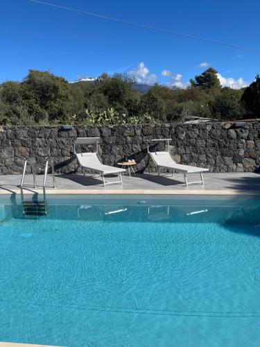 a swimming pool with two chairs and a stone wall at Casa Perla dell'Etna in Ragalna
