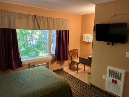 a hotel room with a bed and a flat screen tv at Arbor Inn Motor Lodge - Weymouth in Weymouth