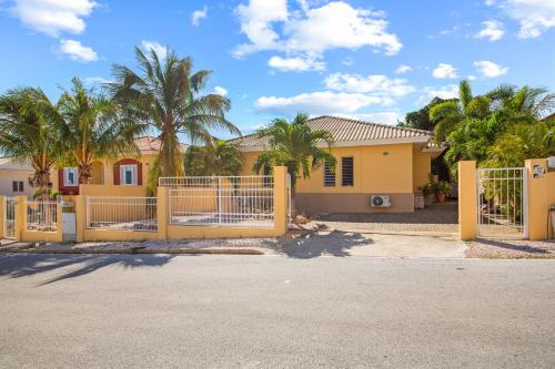 a yellow house with a gate and palm trees at Villa Rubio in Grote Berg