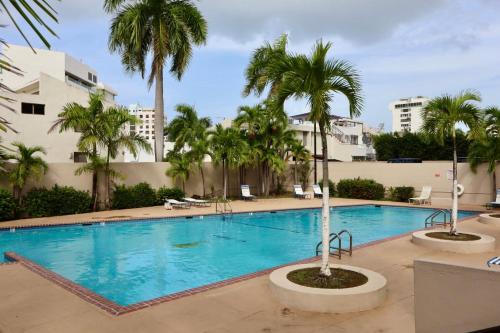 a large swimming pool with palm trees and buildings at Isla Verde Modern Apartment with Pool in San Juan