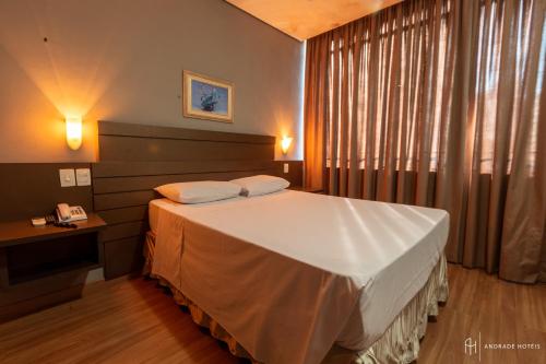 a bedroom with a bed and a window with a phone at Rede Andrade Guaíra in Curitiba