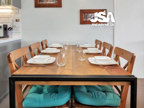 a wooden table with chairs and plates and glasses at Birralee 1 in Jindabyne