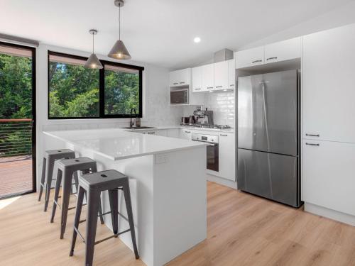 a white kitchen with a large white counter and stools at Casa Della Vita in Jindabyne