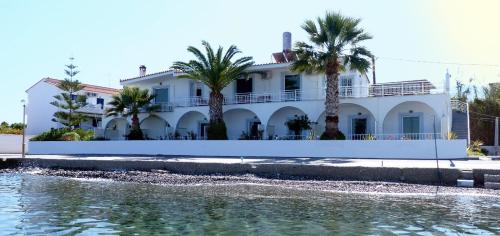 a white house with palm trees in front of a body of water at Manthos in Kalloni