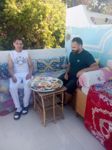 two men sitting on a couch with a table with a tray of food at Nubian Life Nile View in Aswan