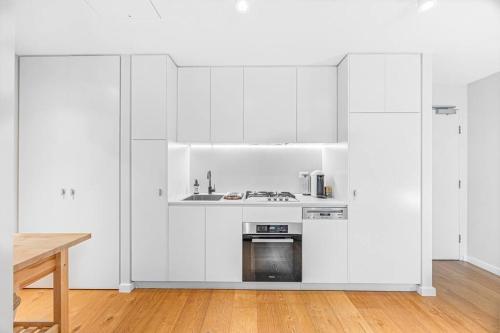 a white kitchen with white cabinets and a wooden floor at Modern & Quiet 1BR Apartment with Private Garden in Bondi close to the Beach in Sydney