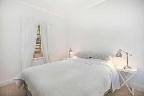 a white bedroom with a white bed and a window at Merri Cottage in Bowral