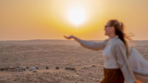 a woman pointing at the sun in the desert at Stars Gate Camp in Al Wāşil