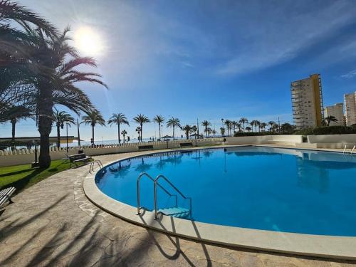 a large blue swimming pool with palm trees and the ocean at Nautico 16 in Benimagrell