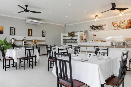 Un restaurante con mesas y sillas blancas y una cocina. en Point R40 Lodge - Conference, Self Catering & Spa, en Nelspruit