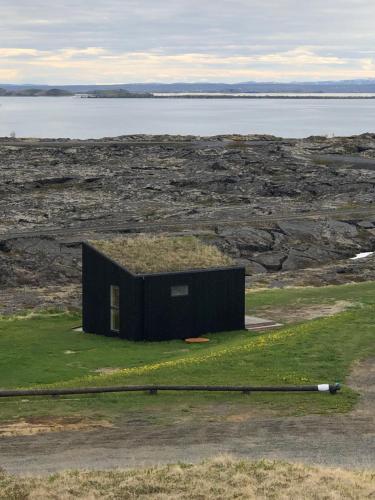 a small black building with a grass roof on a field at Aska, Modern Cabin in Myvatn