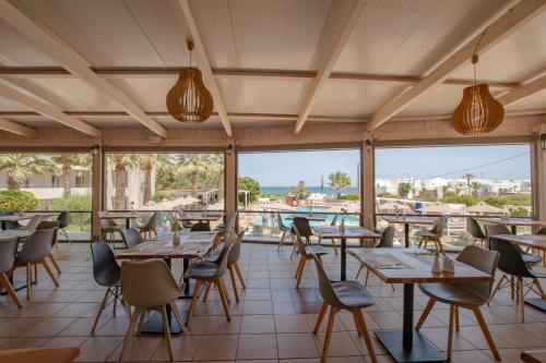 a restaurant with wooden tables and chairs and windows at Gouves Bay by Omilos Hotels in Gouves