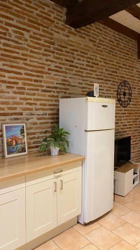 Il comprend une cuisine dotée d'un réfrigérateur blanc et d'un mur en briques. dans l'établissement Le Gite d Eugenie, à Gaillac