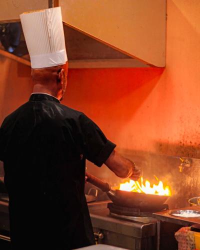 a chef cooking food in a pot on a stove at Royal Crown Residency Hotel in Talawatugoda