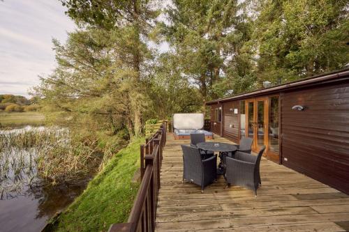 a deck with a table and chairs next to a lake at Buzzard Lodge with Hot-tub in Carlisle