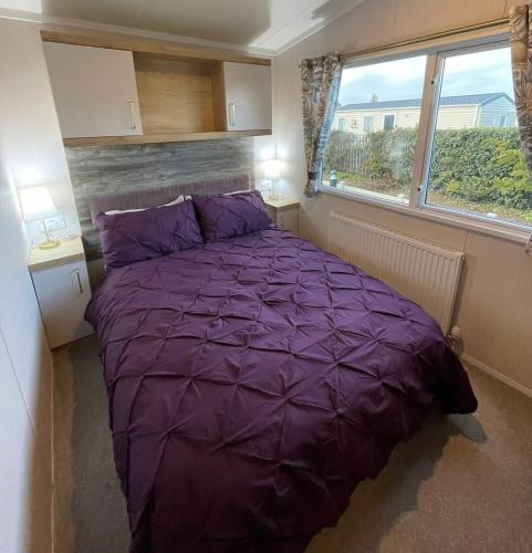 a purple bed in a small room with a window at Golden Palm Resort - Bordeaux Deluxe - Coastal Caravan Breaks in Chapel Saint Leonards
