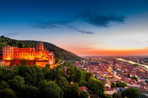 a castle on a hill with a city at sunset at Hotel Goldene Rose in Heidelberg