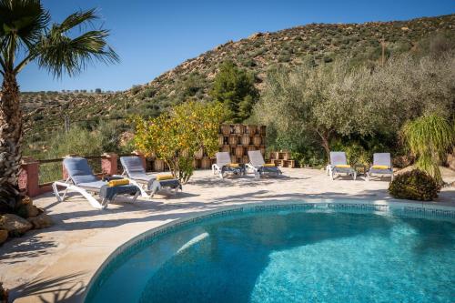 a swimming pool with chaises and chairs next to a mountain at Finca Gran Cerros in Alora