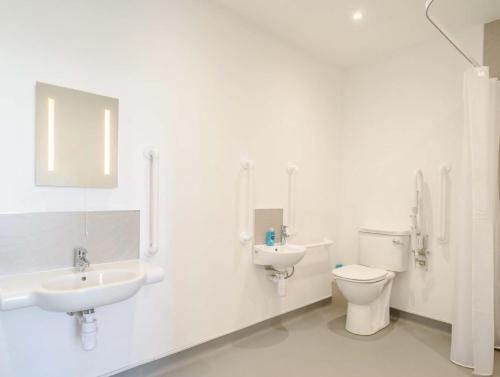 a white bathroom with two sinks and a toilet at Tommy Jacks Beach Apartments in Bude