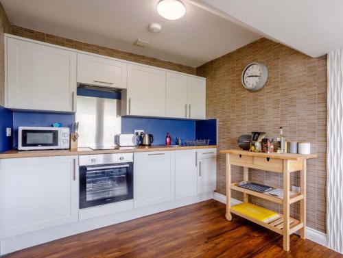 a kitchen with white cabinets and a clock on the wall at Tommy Jacks Beach Apartments in Bude