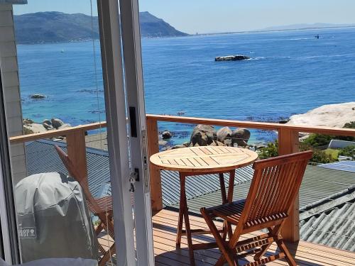 a table and chairs on a balcony with the ocean at Penguins View Guesthouse in Simonʼs Town