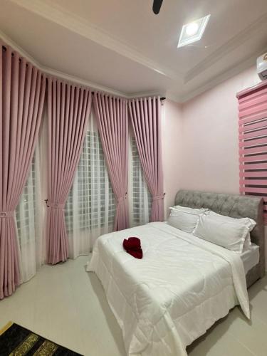 a bedroom with a white bed with pink curtains at Homestay Pulau Serai in Kampong Nibong