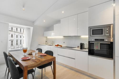 a white kitchen with a wooden table and chairs at Les Deux Mariettes Apartments & Suites in Lisbon