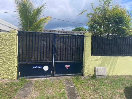 a fence with a black gate with a palm tree behind it at Maison proche aéroport Abymes in Belle-Plaine