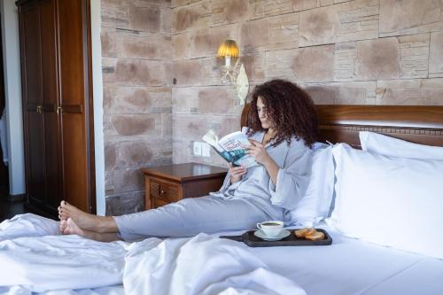 a woman sitting on a bed reading a book at Alseides Boutique Hotel & Spa in Elatochori