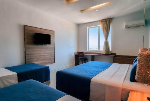 a bedroom with two beds and a desk and a window at Paradiso Corporate in Cabo Frio