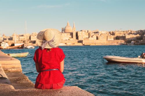 a girl in a red dress and hat looking at the water at Authentic Maltese Boutique Holiday Home with Rooftop Pool - Moon Townhouse in Cospicua