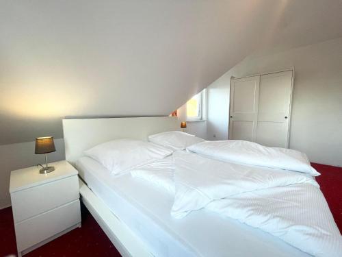 a white bed with white sheets and a night stand at Ferienhaus-Haus-Eversand in Cuxhaven