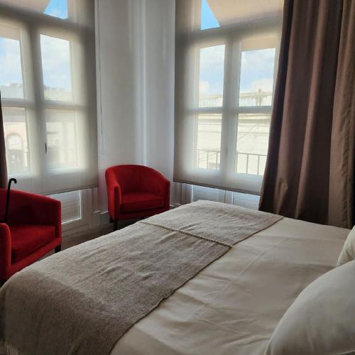 a bedroom with a bed and two chairs and windows at Real Hotel Luján in Luján