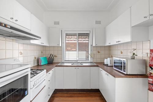 a white kitchen with white appliances and a window at Bright Queen Room - Central Location at Ryde - Shared Bathroom in Sydney