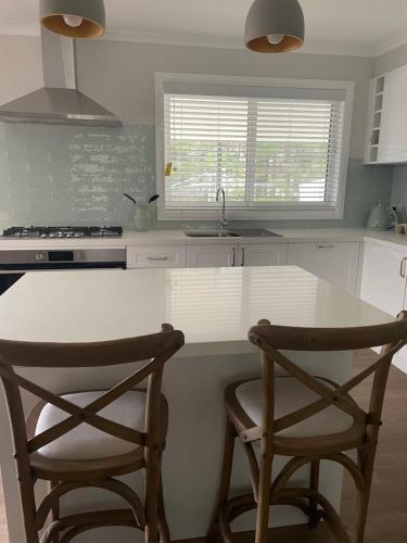 a kitchen with a white counter and two chairs at Cottage amongst the Pines in Wamboin