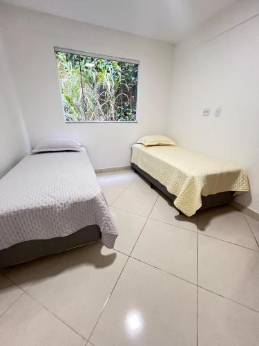 deux lits dans une chambre blanche avec une fenêtre dans l'établissement Apartamento com 3 quartos no centro de Domingos Martins, à Domingos Martins