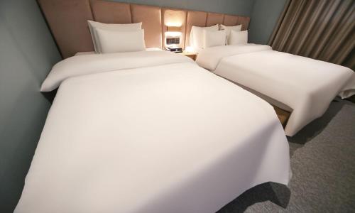 two beds in a hotel room with white sheets at From H Lazy Heaven in Changwon