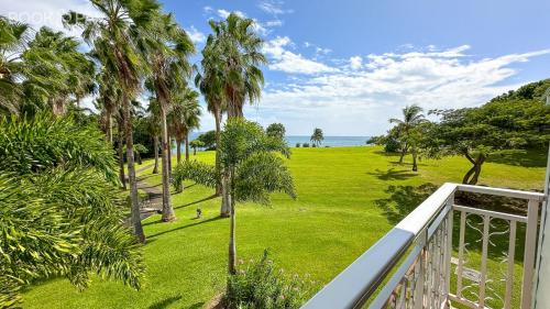 a balcony view of a park with palm trees and the ocean at Studio O'PALM in Sainte-Luce